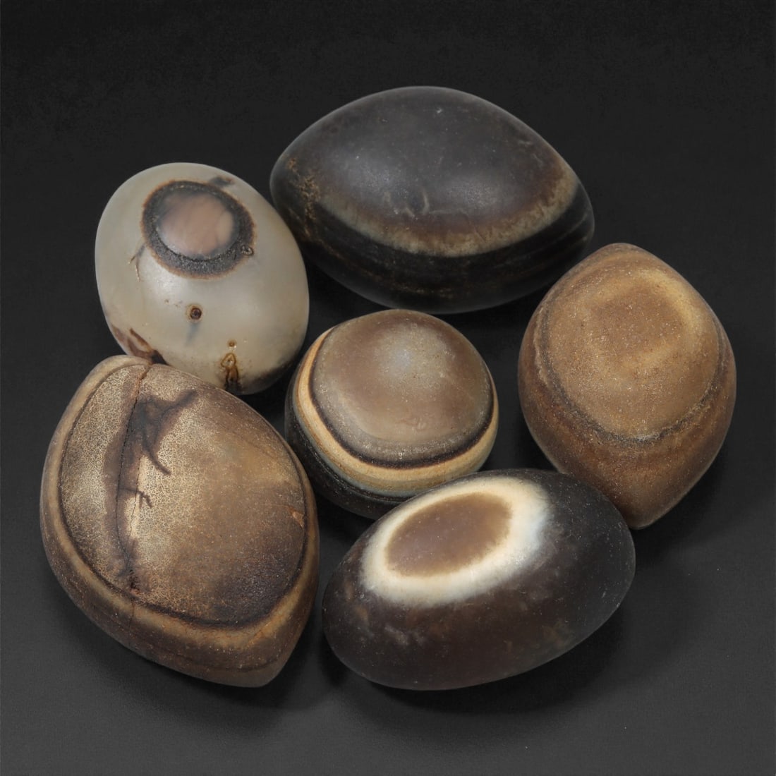 A Group of Tibetan Stone Luk Mik ("Goat Eye") Beads, 19th-Early 20th Century, 15LG: Carved from banded agate and chalcedony, the group comprises six domed, oval, and lenticular beads characterized by concentric circular banding that creates the "eye" motif associated with luk mik for
