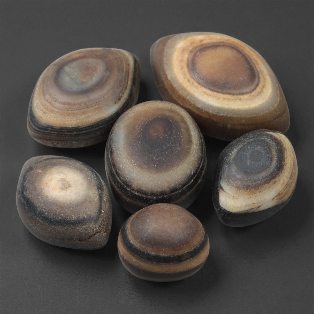 A Group of Tibetan Stone Luk Mik ("Goat Eye") Beads, 19th-Early 20th Century, 11LG: Carved from banded agate and chalcedony, the group comprises six domed, oval, and lenticular beads characterized by concentric circular banding that creates the "eye" motif associated with luk mik for