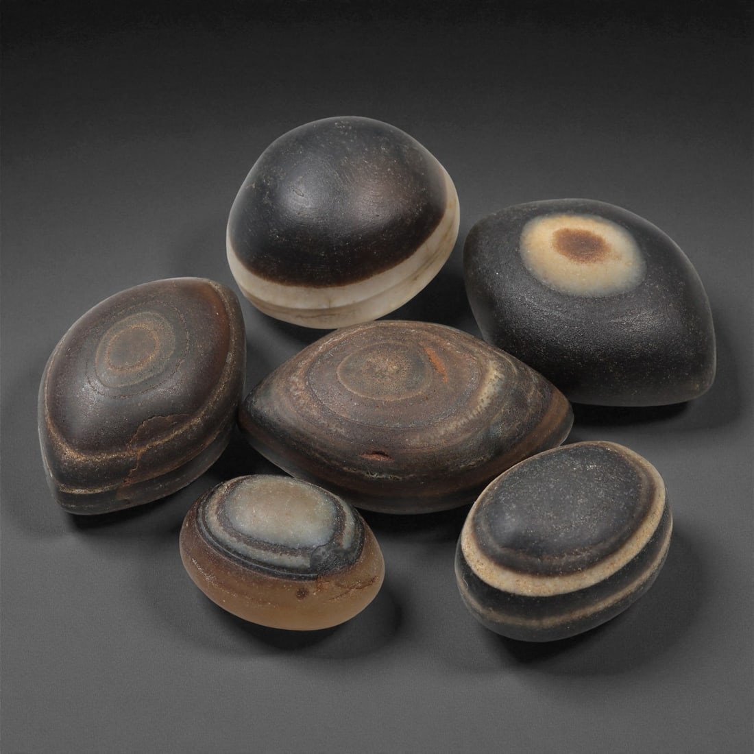 A Group of Tibetan Stone Luk Mik ("Goat Eye") Beads, 19th-Early 20th Century, 20LG: Carved from banded agate and chalcedony, the group comprises six domed, oval, and lenticular beads characterized by concentric circular banding that creates the "eye" motif associated with luk mik for