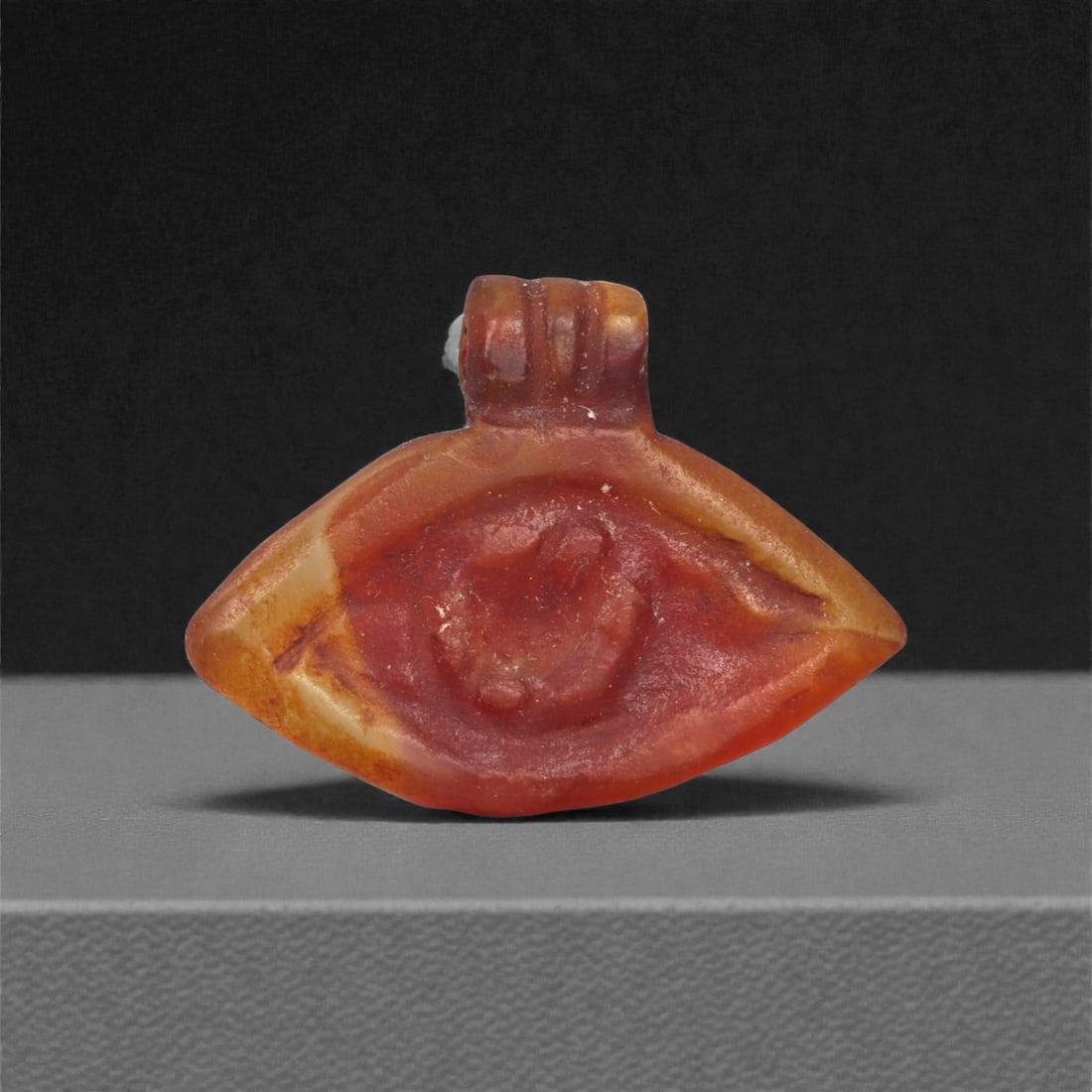 An Egyptian Carnelian Amulet, Coptic Period, 4th-7th Century CE, 2cm, 14LJ: Worked from orange carnelian with natural internal variation, the amulet shows a compact form with smoothed contours and modest surface definition. Light wear is visible along the edges. Objects of th