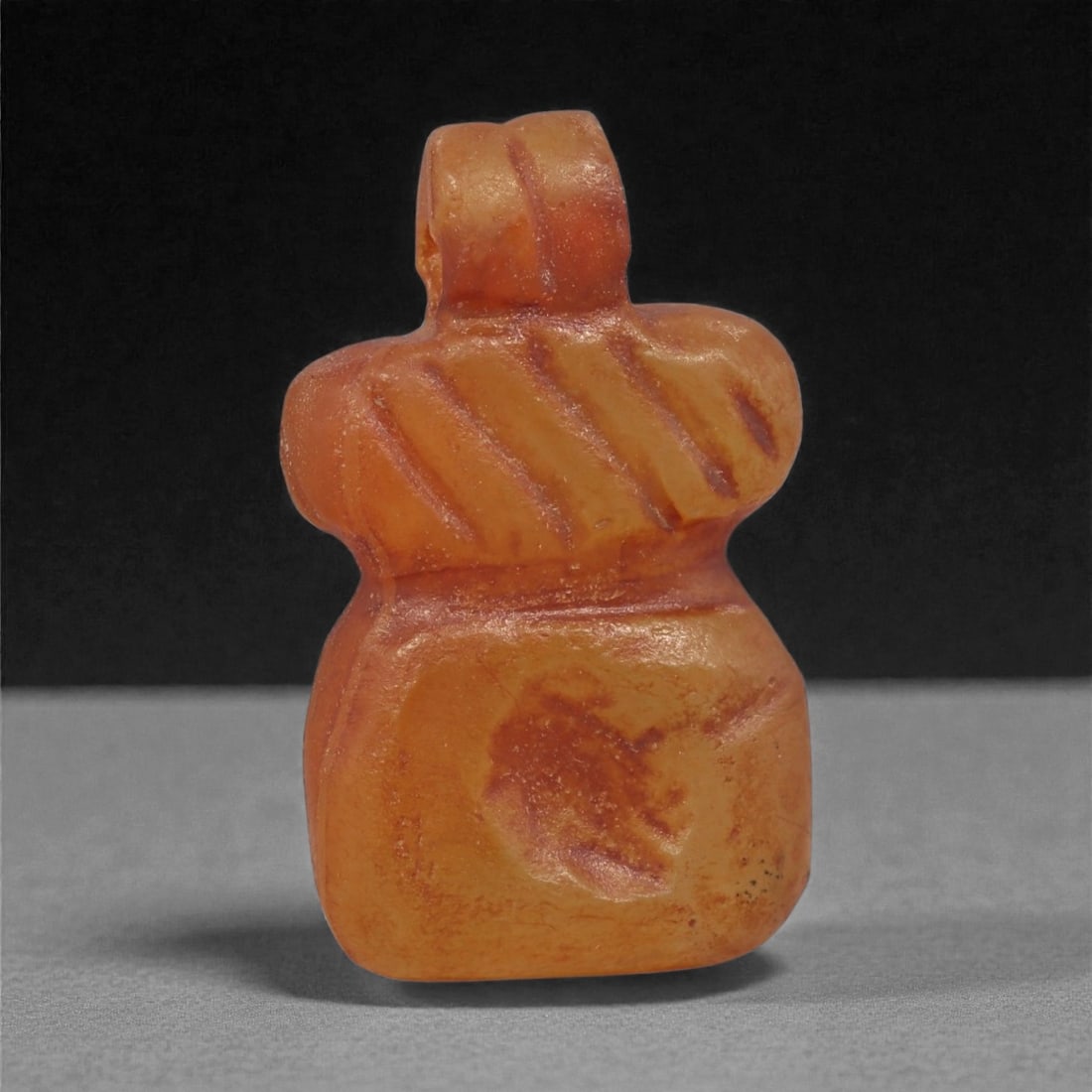 An Egyptian Carnelian Amulet, Coptic Period, 4th-7th Century CE, 1.9cm, 37LK: Worked from orange carnelian with natural internal variation, the amulet shows a compact form with smoothed contours and modest surface definition. Light wear is visible along the edges. Objects of th