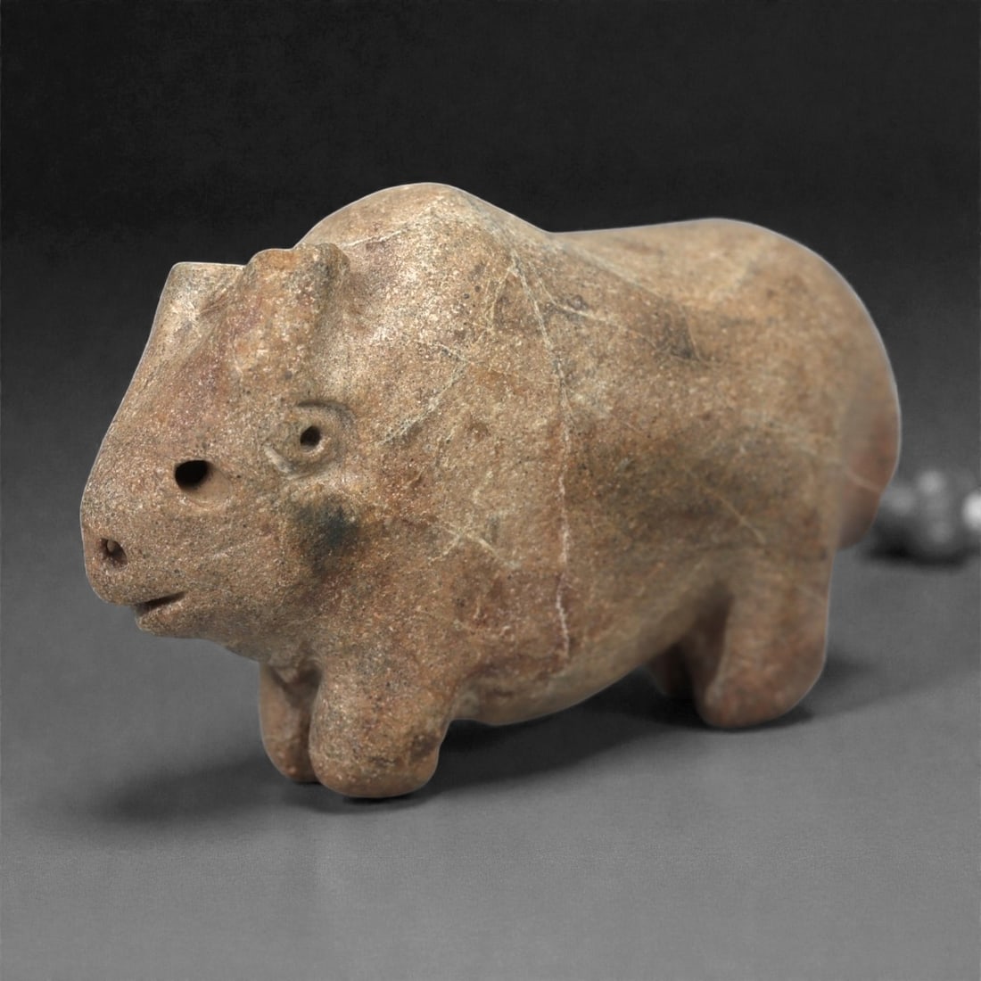 A Near Eastern Stone Bovid Figurine, 3rd-2nd Millennium BCE, 96LA: Carved from a mottled brown stone with natural surface veining, the figure is modeled in the round with a compact body supported on four short legs. The head is rendered with a broad snout, small dril