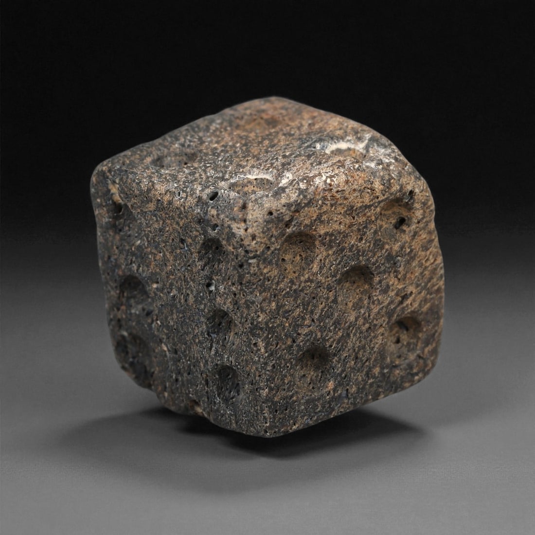 A Roman Bone Gaming Die, 1st-3rd Century CE, 93ZA: Carved from dense bone, the object is shaped as a small cube with slightly rounded edges. Each face bears a series of drilled circular pips arranged in standard numerical configurations. The surfaces 