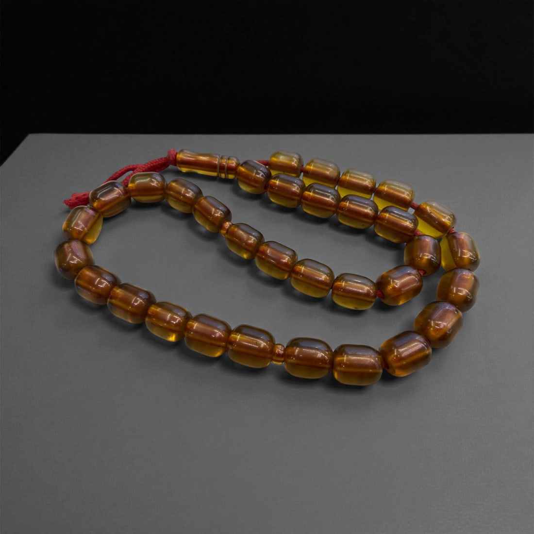 An Amber Mala Prayer Bead Strand, Mid-20th Century, 97g, 47EE: Composed of cylindrical amber beads in uniform warm brown tones, the strand is arranged as a continuous mala with a larger terminal bead and adjacent cylindrical counters. The beads are smoothly polis