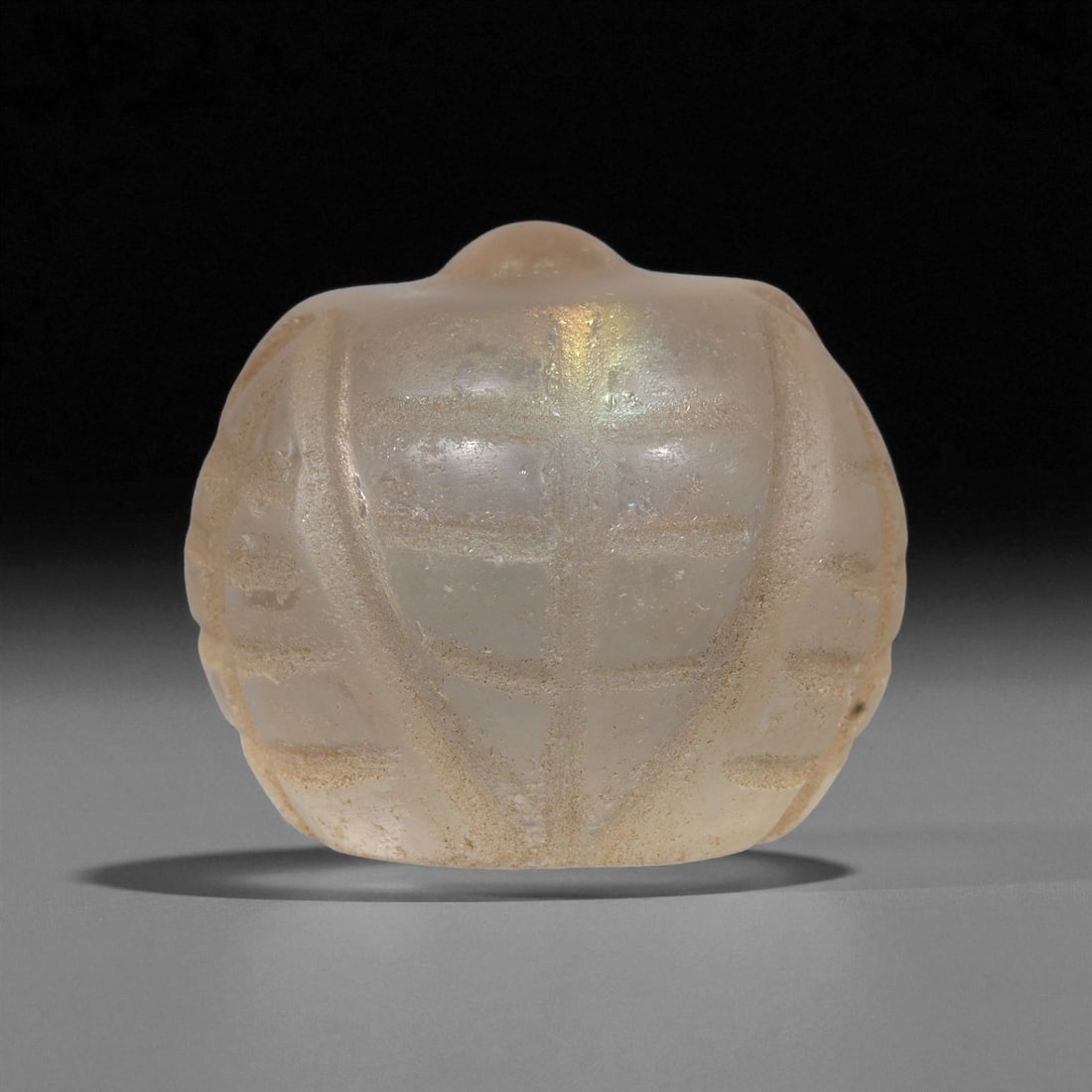 A Coptic Glass Carved Element, 4th-7th Century CE, 23LF: Formed from translucent glass with a pale, slightly iridescent surface, the object is shaped as a rounded form with a raised central knob. Linear grooves are cut across the surface, creating a segment