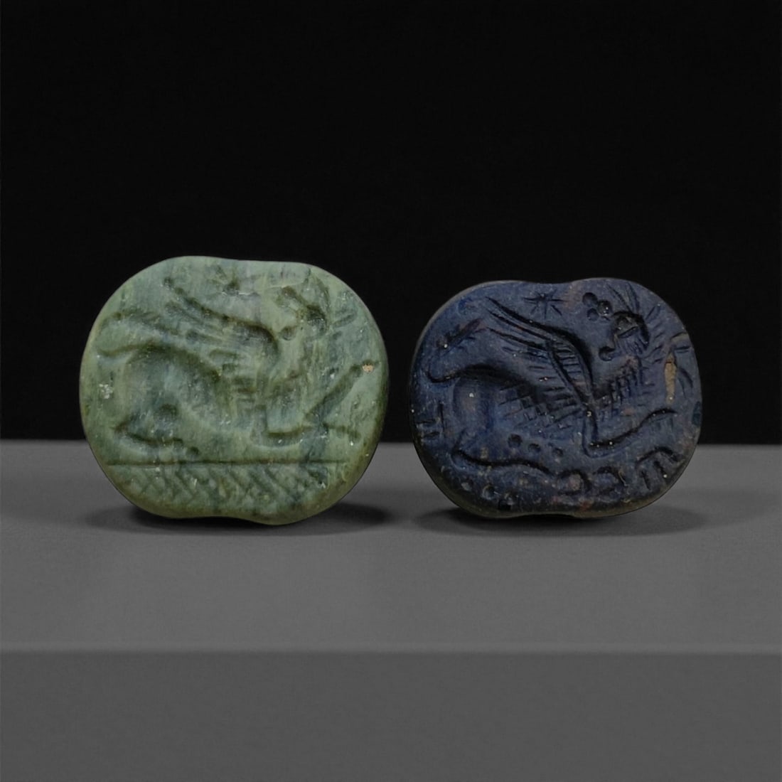 A Parthian-Roman Hemispherical Stamp Seals with Winged Griffin, c. 2nd Century CE, 2cm, 11g, 80AA: This finely preserved pair of hemispherical stamp seals, carved from green and deep blue stone respectively, dates to the cultural fusion of the Parthian and Roman worlds between the 1st century BCE a