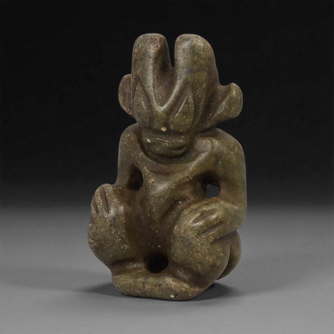 A Chinese Jade Effigy in Hongshan Style, 20th Century, 96LE: Carved from mottled green jade with brown inclusions, the figure depicts a seated anthropomorphic form with bent legs and arms resting on the knees. The head is shaped with a bifurcated crest, flaring