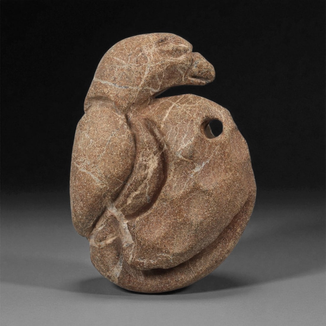 A Near Eastern Stone Bird Pendant, 3rd-2nd Millennium BCE, 37LA: Carved from brown stone with lighter surface veining, the pendant depicts a bird with a compact, rounded body and a pronounced curved wing rendered in shallow relief along one side. The head is turned