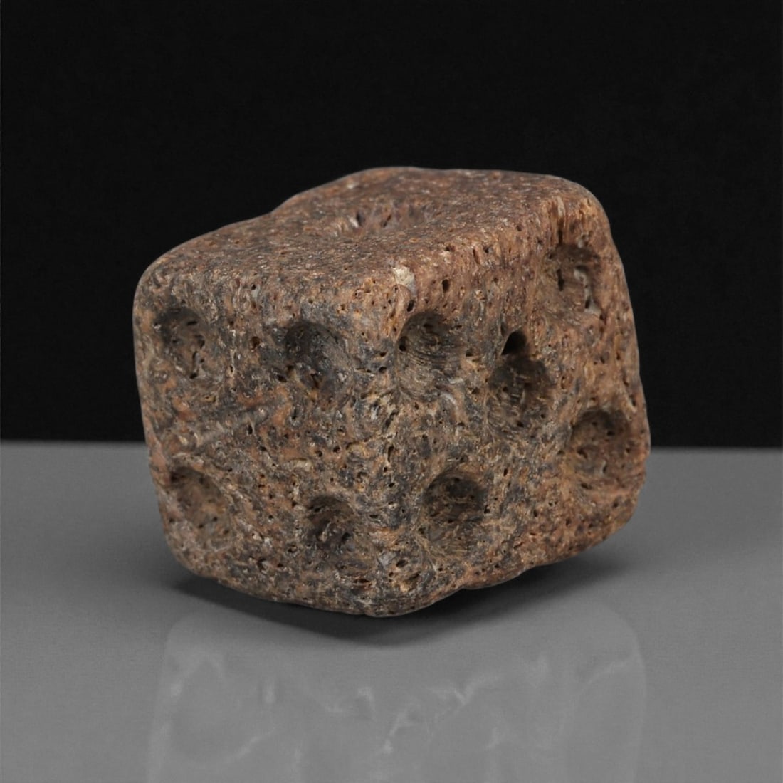 A Roman Bone Gaming Die, 1st-3rd Century CE, 57ZB: Carved from dense bone, the object is shaped as a small cube with slightly rounded edges. Each face bears a series of drilled circular pips arranged in standard numerical configurations. The surfaces 