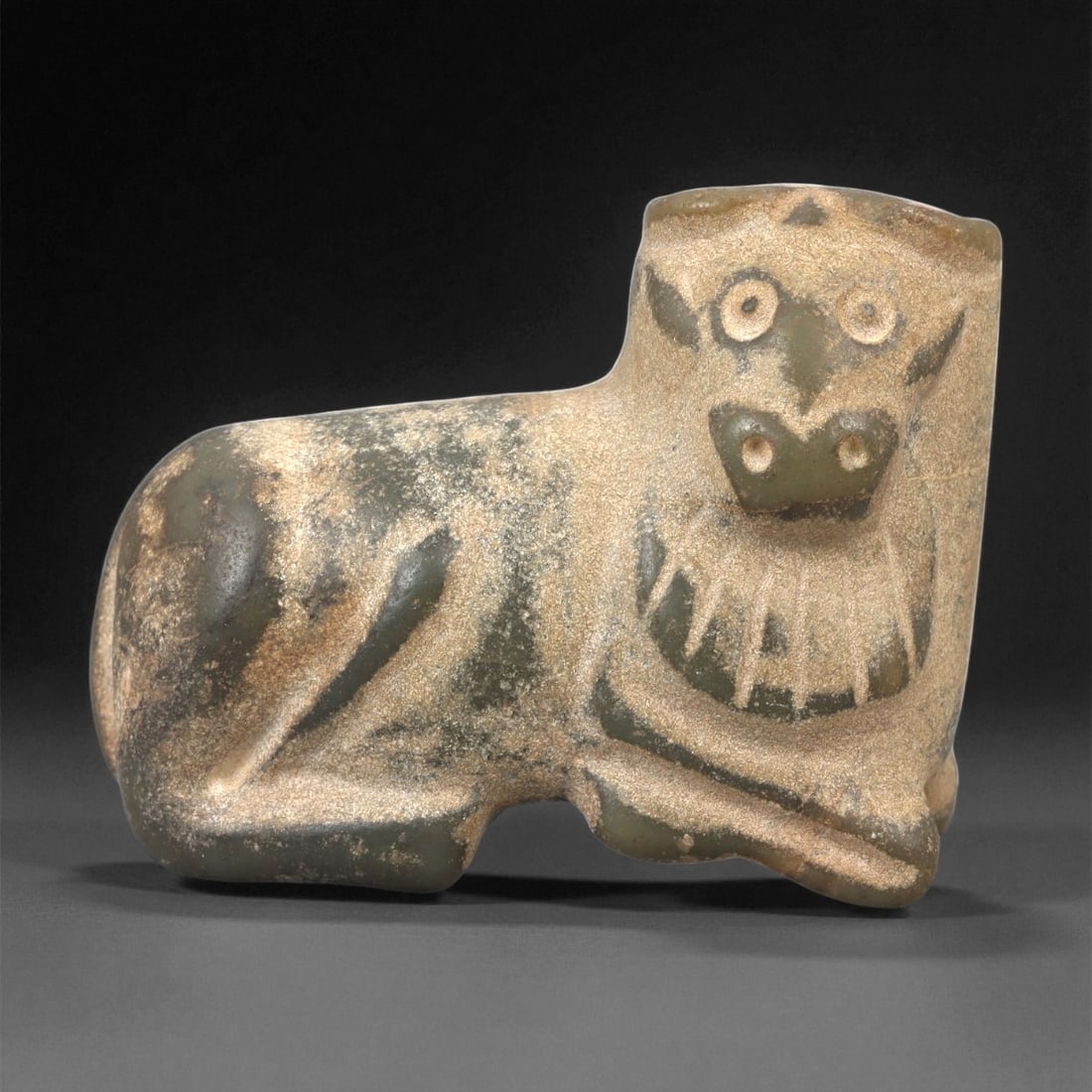 A Mesopotamian Stone Bovid Effigy, 3rd-2nd Millennium BCE, 78LE: Carved from a dark greenish stone with lighter surface accretions, the object represents a recumbent bovid with the forelegs folded beneath the body. The head is upright with a squared muzzle, recesse