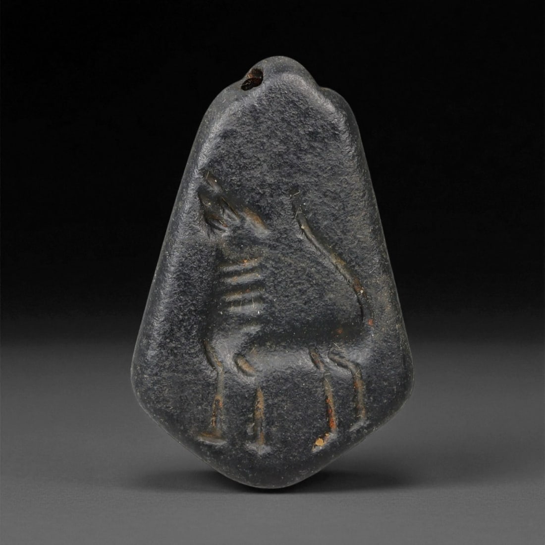 Ancient Neo-Babylonian Steatite Gazelle Motif Amulet Pendant, c. 7th-6th Century BCE, 4cm, 24EQ: This pendant, carved from dark steatite, dates to the Neo-Babylonian period, c. 7th-6th century BCE. Pierced at the top for suspension, it was designed as a personal amulet to be worn close to the bod