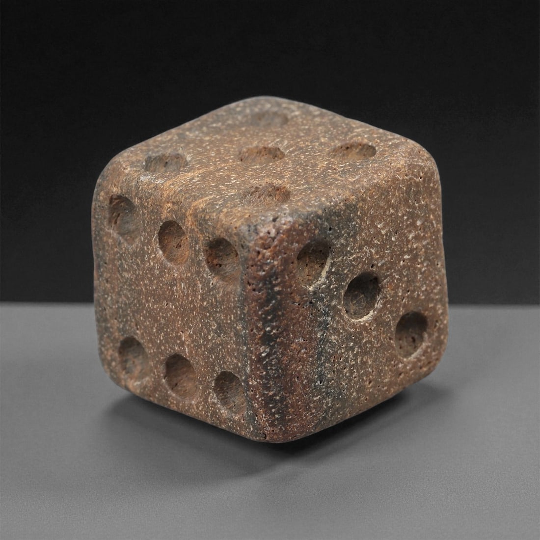 A Roman Bone Gaming Die, 1st-3rd Century CE, 80LD: Carved from light brown bone with a porous, naturally textured surface, the cubic die bears circular recessed pips on each face arranged in standard numerical configurations. The edges are slightly ro