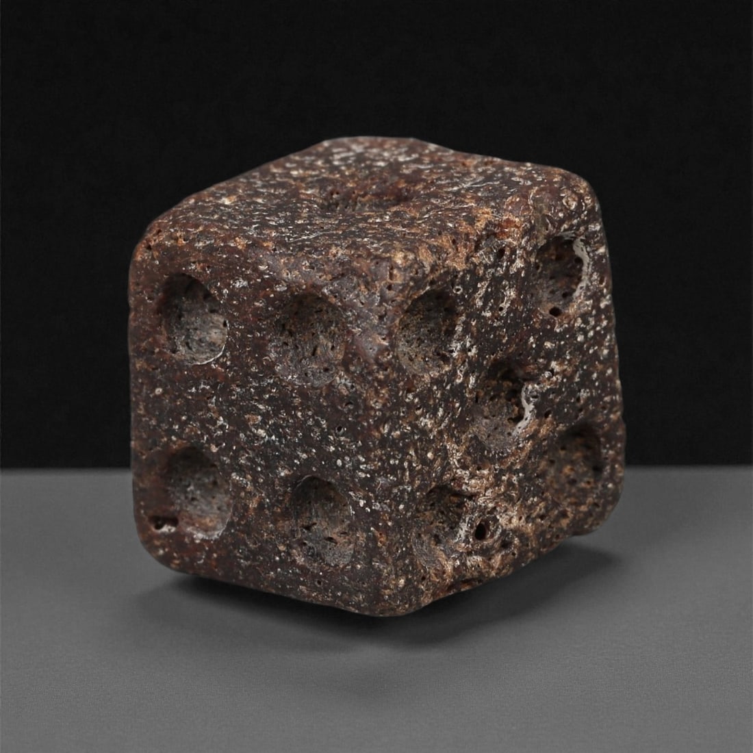 A Roman Bone Gaming Die, 1st-3rd Century CE, 73ZA: Carved from dense bone, the object is shaped as a small cube with slightly rounded edges. Each face bears a series of drilled circular pips arranged in standard numerical configurations. The surfaces 