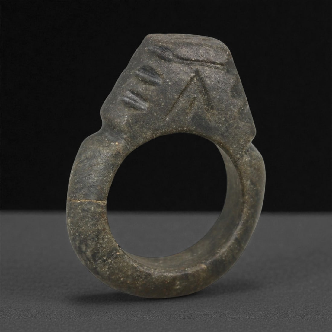 A Parthian Steatite Signet Ring with Stylized Intaglio, c. 2nd-3rd Century CE, 3.9cm, 12.6g, 3LH: This substantial signet ring, carved from dark steatite. Its heavy bezel is engraved with stylized intaglio imagery, likely representing symbolic motifs used for personal or administrative sealing. Th