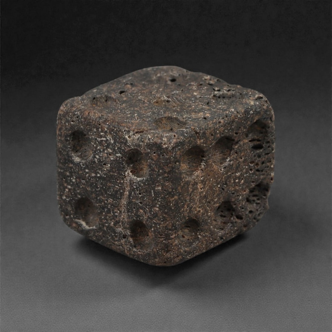 A Roman Bone Gaming Die, 1st-3rd Century CE, 1.5cm, 61LG: Carved from dense bone, the object is shaped as a small cube with slightly rounded edges. Each face bears a series of drilled circular pips arranged in standard numerical configurations. The surfaces 