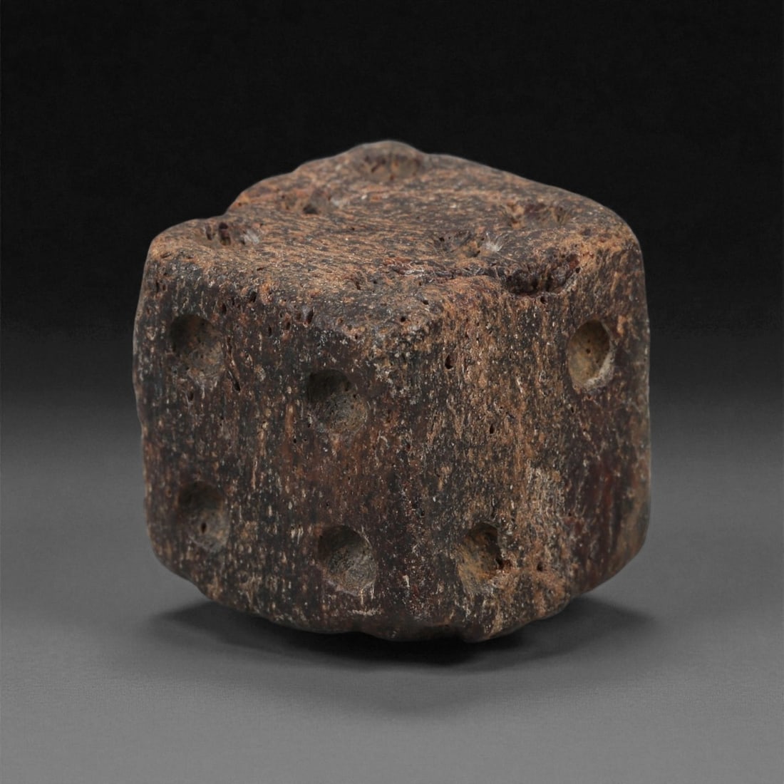 A Roman Bone Gaming Die, 1st-3rd Century CE, 1.7cm, 59LG: Carved from dense bone, the object is shaped as a small cube with slightly rounded edges. Each face bears a series of drilled circular pips arranged in standard numerical configurations. The surfaces 