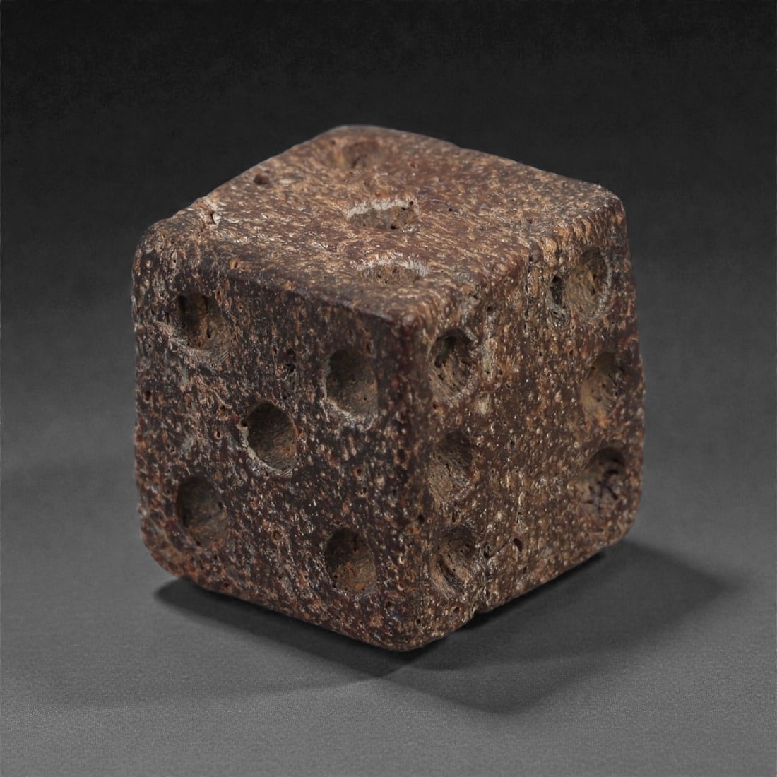 A Roman Bone Gaming Die, 1st-3rd Century CE, 1.5cm, 67LG: Carved from dense bone, the object is shaped as a small cube with slightly rounded edges. Each face bears a series of drilled circular pips arranged in standard numerical configurations. The surfaces 