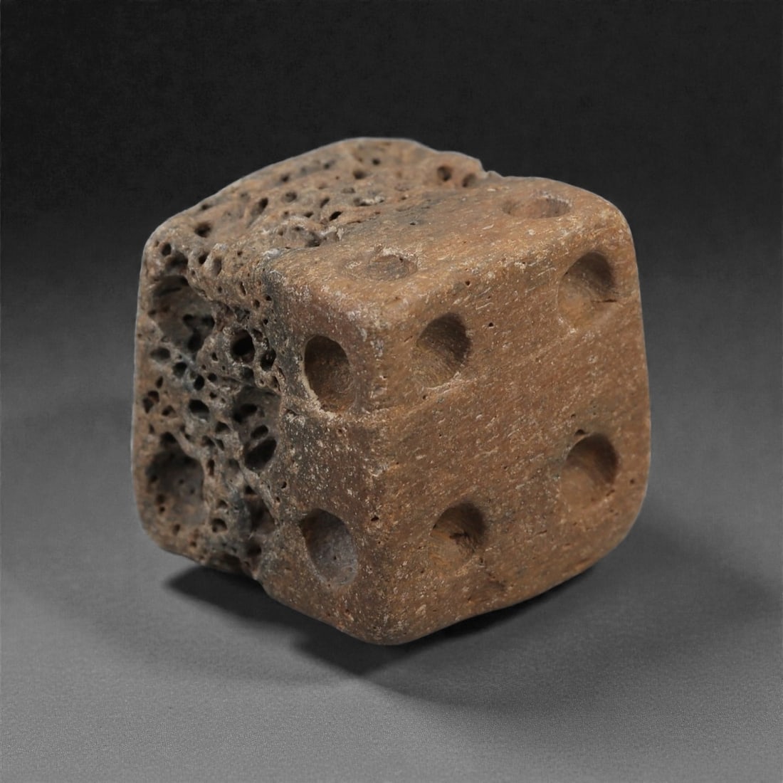 A Roman Bone Gaming Die, 1st-3rd Century CE, 1.5cm, 63LG: Carved from dense bone, the object is shaped as a small cube with slightly rounded edges. Each face bears a series of drilled circular pips arranged in standard numerical configurations. The surfaces 