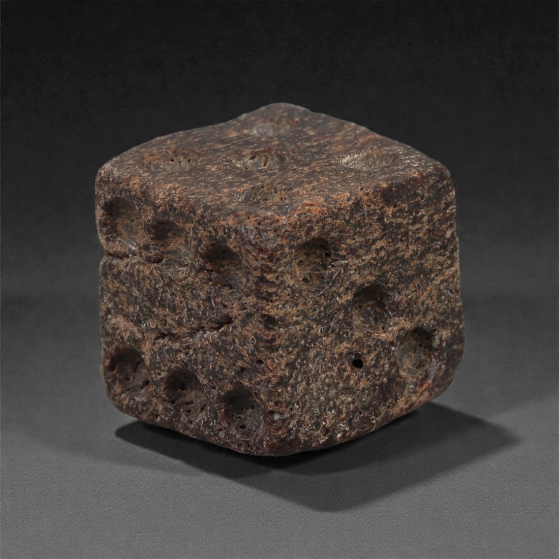 A Roman Bone Gaming Die, 1st-3rd Century CE, 1.5cm, 66LG: Carved from dense bone, the object is shaped as a small cube with slightly rounded edges. Each face bears a series of drilled circular pips arranged in standard numerical configurations. The surfaces 