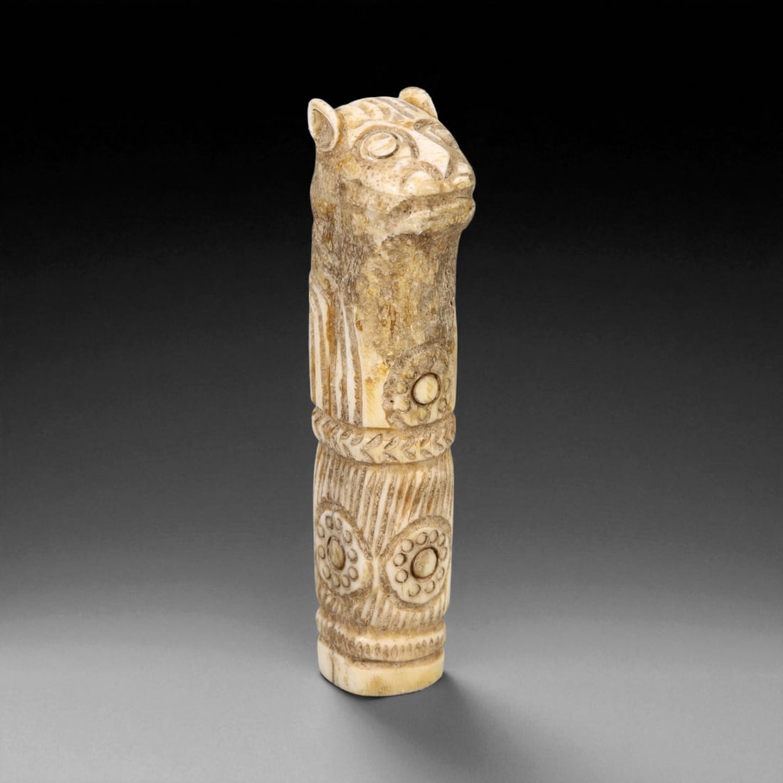 A Parthian Carved Bone Finial in the Form of a Feline, ca. 1st Century BCE, 74WC: Carved from a warm beige bone with naturally variegated surface tones, the finial is sculpted as a standing feline with upright ears, large circular eyes, and a tapered snout. The elongated neck desce