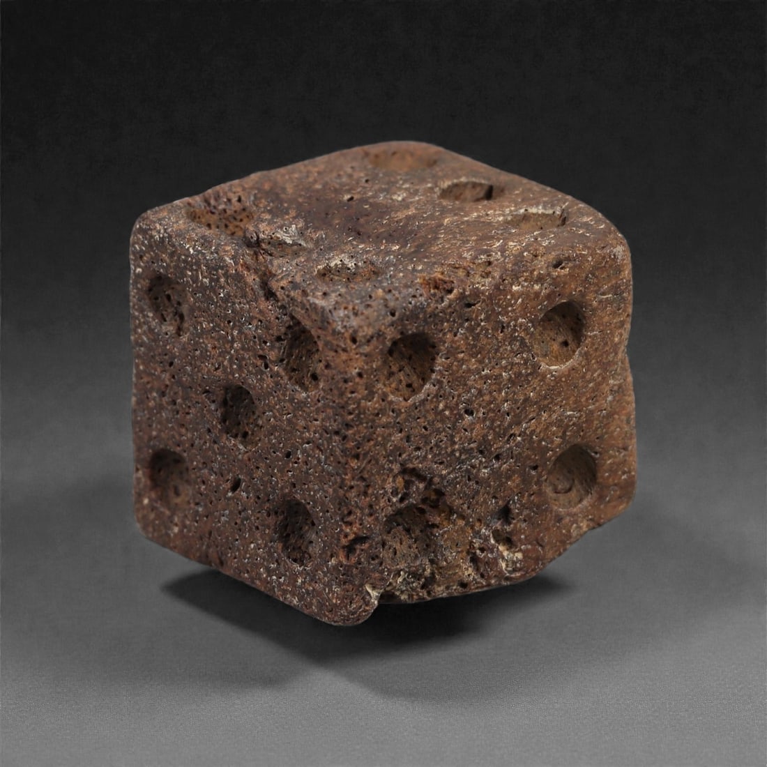 A Roman Bone Gaming Die, 1st-3rd Century CE, 1.7cm, 68LG: Carved from dense bone, the object is shaped as a small cube with slightly rounded edges. Each face bears a series of drilled circular pips arranged in standard numerical configurations. The surfaces 