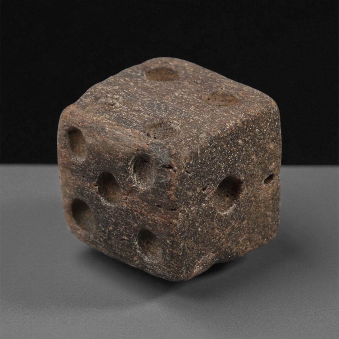 A Roman Bone Gaming Die, 1st-3rd Century CE, 1.5cm, 60LG: Carved from dense bone, the object is shaped as a small cube with slightly rounded edges. Each face bears a series of drilled circular pips arranged in standard numerical configurations. The surfaces 