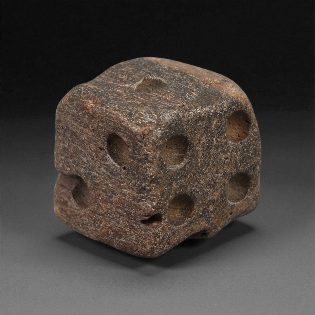 A Roman Bone Gaming Die, 1st-3rd Century CE, 1.4cm, 56LG: Carved from dense bone, the object is shaped as a small cube with slightly rounded edges. Each face bears a series of drilled circular pips arranged in standard numerical configurations. The surfaces 