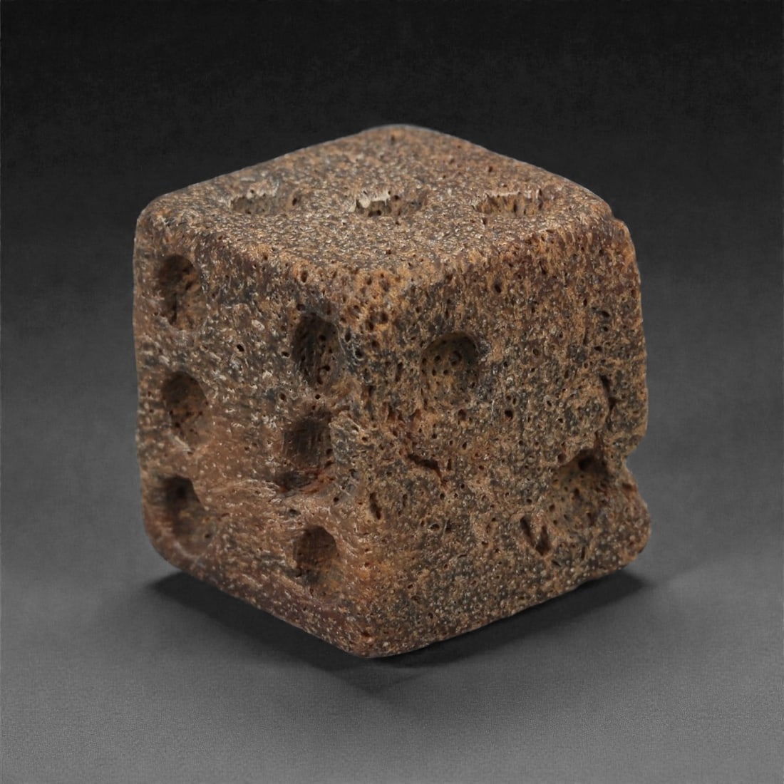 A Roman Bone Gaming Die, 1st-3rd Century CE, 1.5cm, 62LG: Carved from dense bone, the object is shaped as a small cube with slightly rounded edges. Each face bears a series of drilled circular pips arranged in standard numerical configurations. The surfaces 