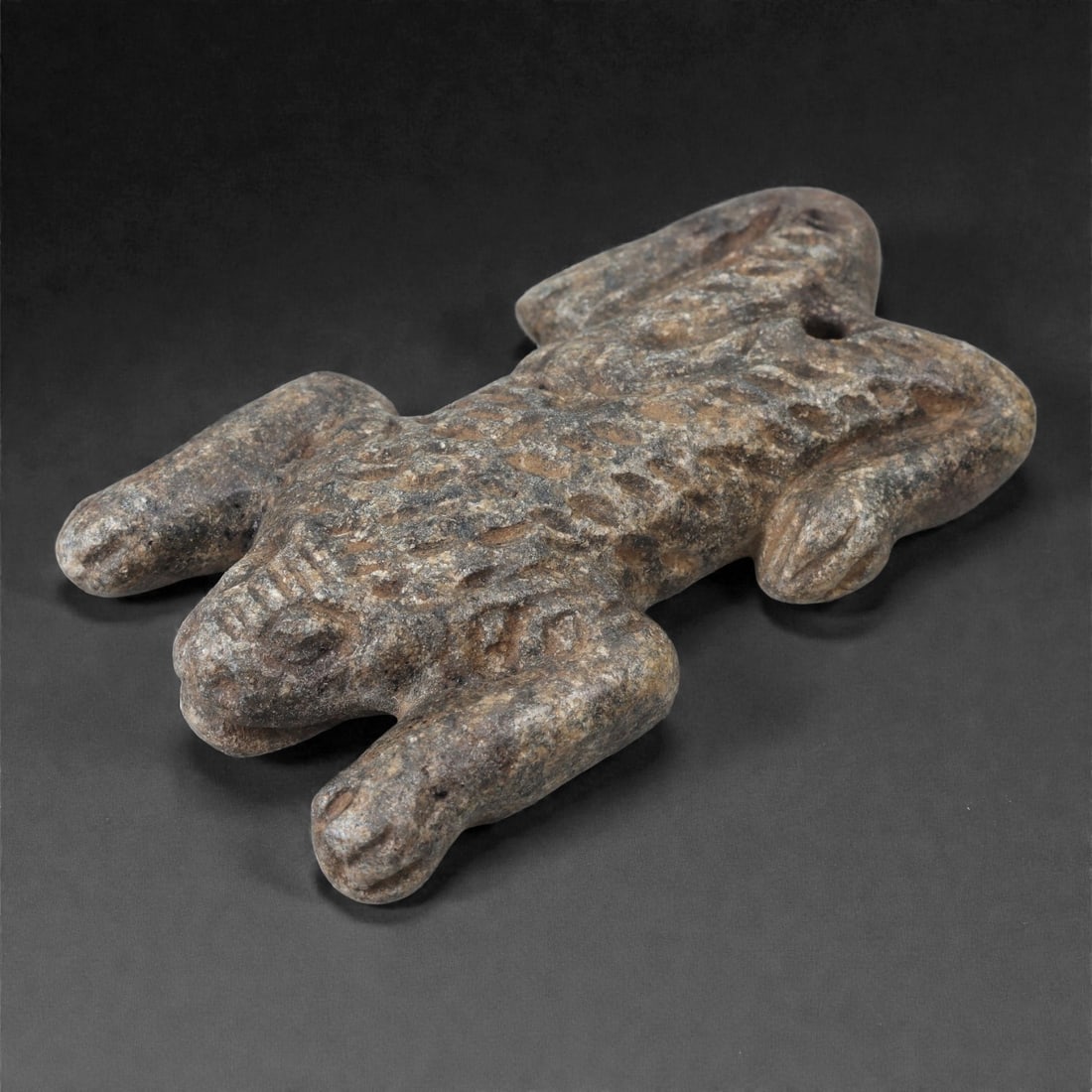 An Anatolian Schist Zoomorphic Figure, Middle Bronze Age, 2nd Millennium BCE, 68LJ: Carved from dark grey schist, the figure depicts a reptilian creature with a broad head, short legs extending outward, and a tapering body. The dorsal surface is covered with pecked circular depressio