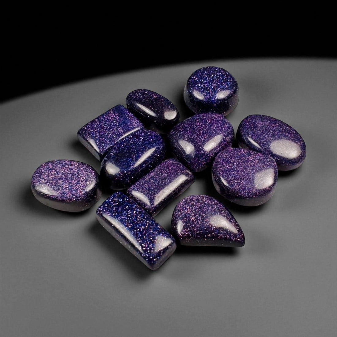 113.55 Carats Midnight Purple Goldstone Cabochon Selection Lot, 49WA: This radiant parcel of midnight purple goldstone cabochons shimmers with a captivating galaxy-like sparkle, each stone alive with fine metallic inclusions that dance beneath the surface. The deep viol