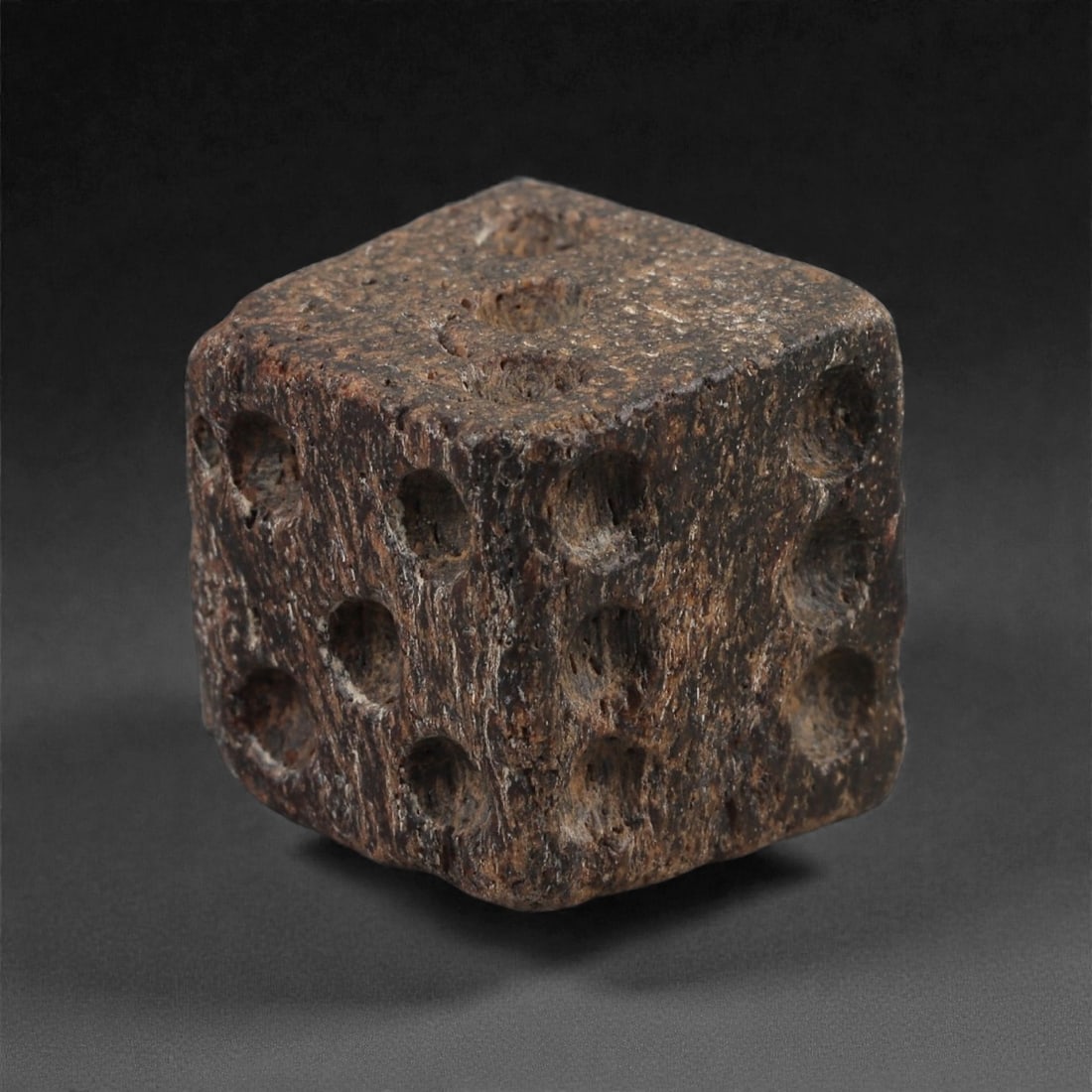 A Roman Bone Gaming Die, 1st-3rd Century CE, 1.4cm, 88AD: Carved from dense bone, the object is shaped as a small cube with slightly rounded edges. Each face bears a series of drilled circular pips arranged in standard numerical configurations. The surfaces 