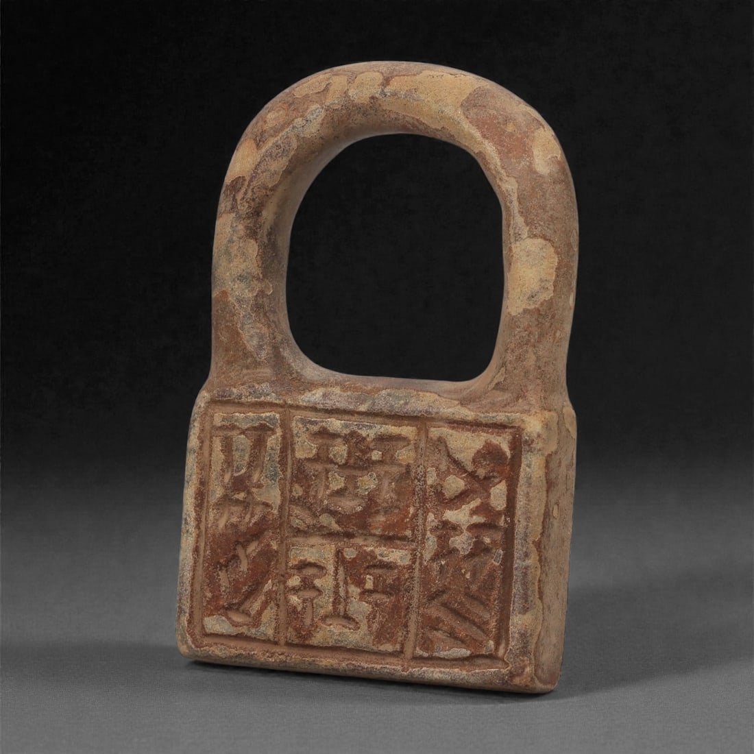 A Mesopotamian Stone Handled Weight, Neo-Babylonian-Achaemenid Period, 6th-4th Century BCE, 23LQ: Carved from mottled brown stone, the object consists of a rectangular lower block surmounted by a thick arched handle shaped from the same piece. The front surface is arranged in four recessed compart