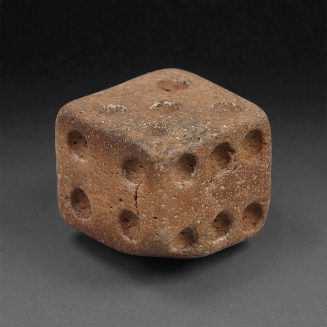 A Roman Bone Gaming Die, 1st-3rd Century CE, 1.4cm, 94AD: Carved from dense bone, the object is shaped as a small cube with slightly rounded edges. Each face bears a series of drilled circular pips arranged in standard numerical configurations. The surfaces 