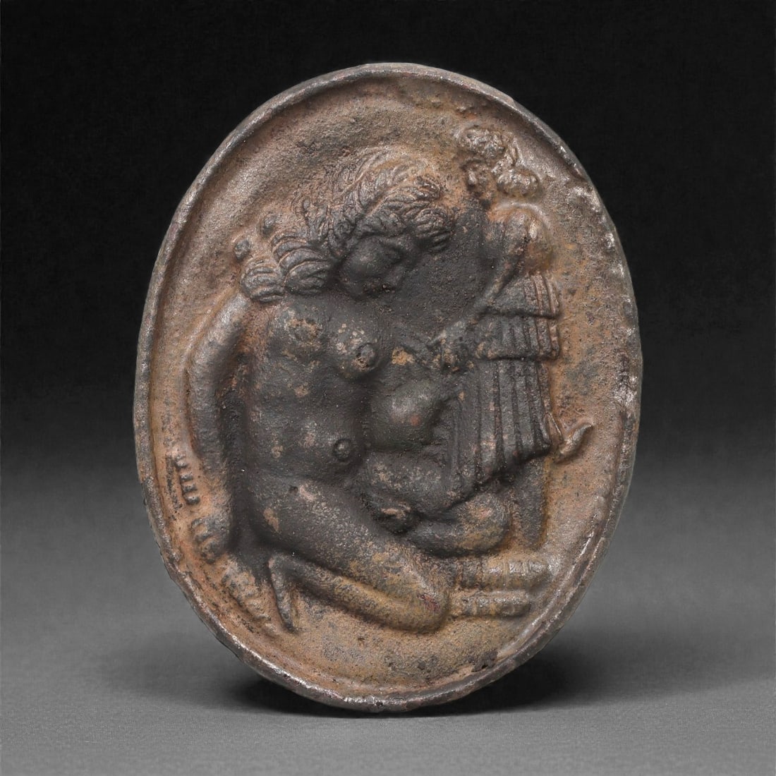 A Roman Provincial Bronze Stamp Seal with Seated Female Figure, 2nd-3rd Century CE, 69LP: Cast in bronze, the oval seal matrix is formed with a recessed figurative scene depicting a seated nude female figure, her body shown in three-quarter view with the head inclined downward. The hair is