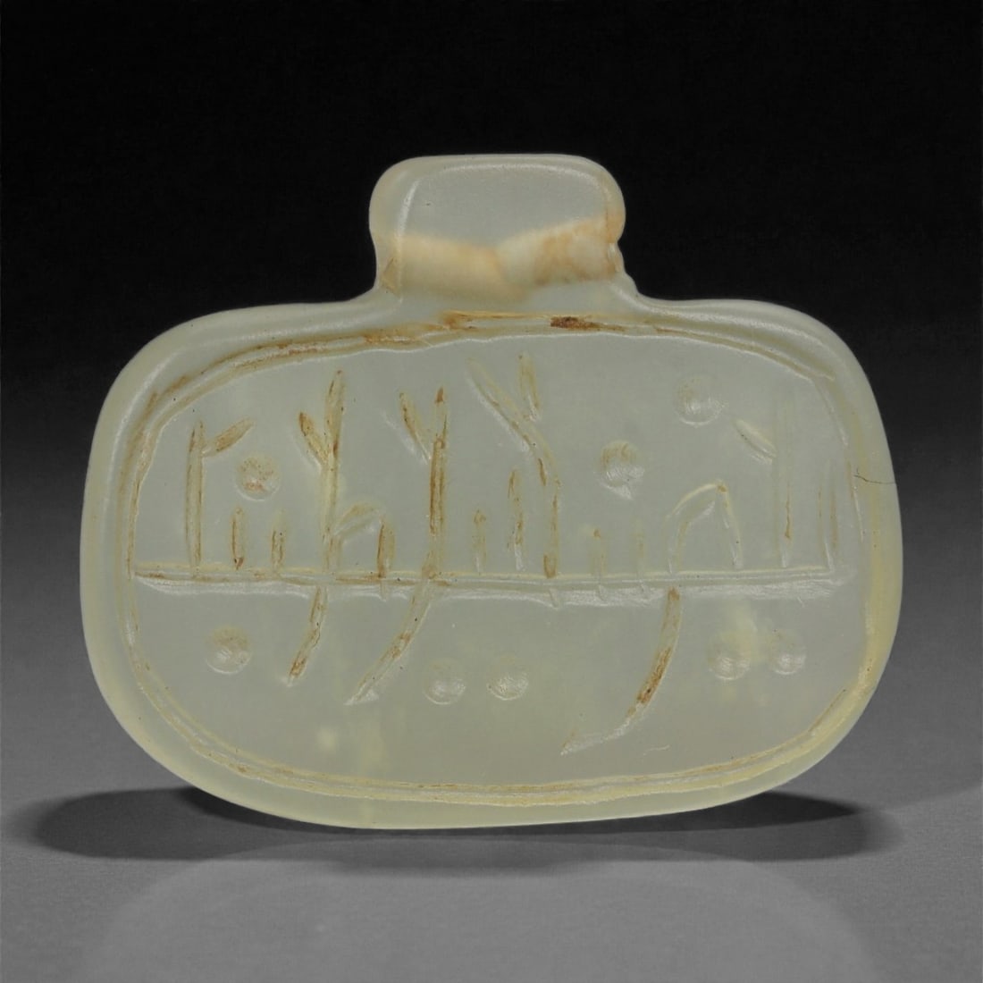 An Islamic Jade Amulet, Medieval Period, 12th-14th Century CE, 91LP: Carved from translucent pale green jade with a faint creamy band across the upper section, the amulet is formed with a rounded rectangular body surmounted by a short integral suspension tab. The front