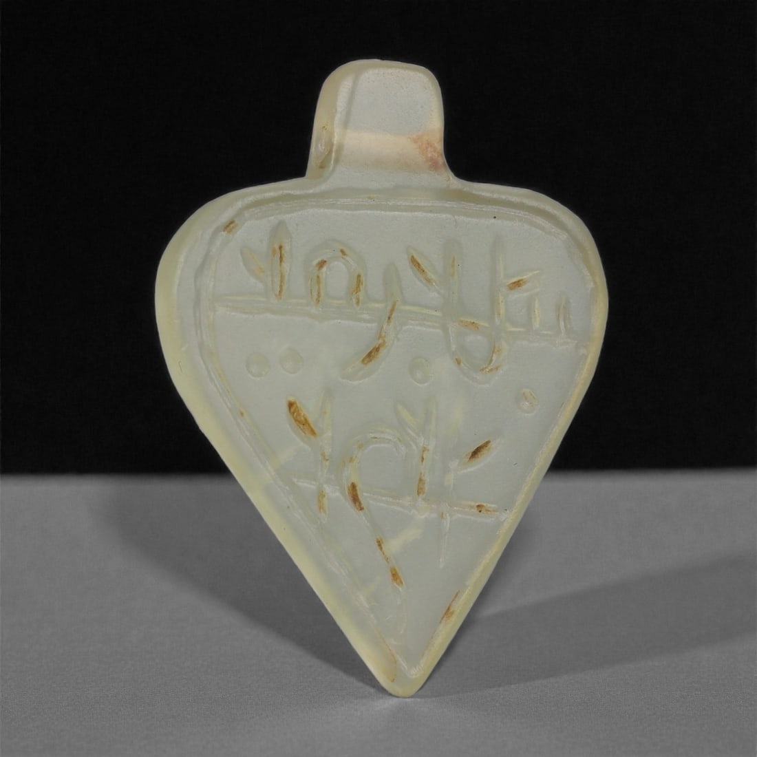 An Islamic Jade Amulet, Medieval Period, 12th-14th Century CE, 93LP: Carved from pale translucent jade, the amulet is formed as an elongated triangular plaque with rounded shoulders and an integral suspension tab above. The front surface bears an incised Arabic inscrip