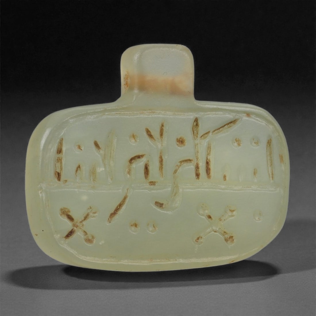An Islamic Jade Amulet, Medieval Period, 12th-14th Century CE, 95LP: Carved from translucent pale green jade, the amulet is shaped with a rounded rectangular body surmounted by a short squared suspension tab. The front surface bears an incised Arabic inscription arrang