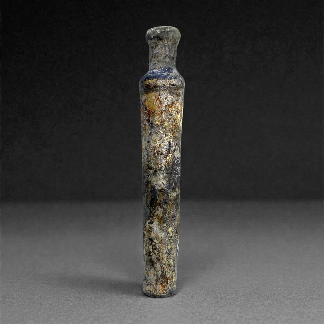 A Roman Levantine Glass Unguentarium, 1st Century CE, 19 g, 56AA: Blown from pale blue-green glass now obscured by dense weathering and mineral accretion, the vessel has a markedly elongated cylindrical body rising into a short, constricted neck with a slightly thic