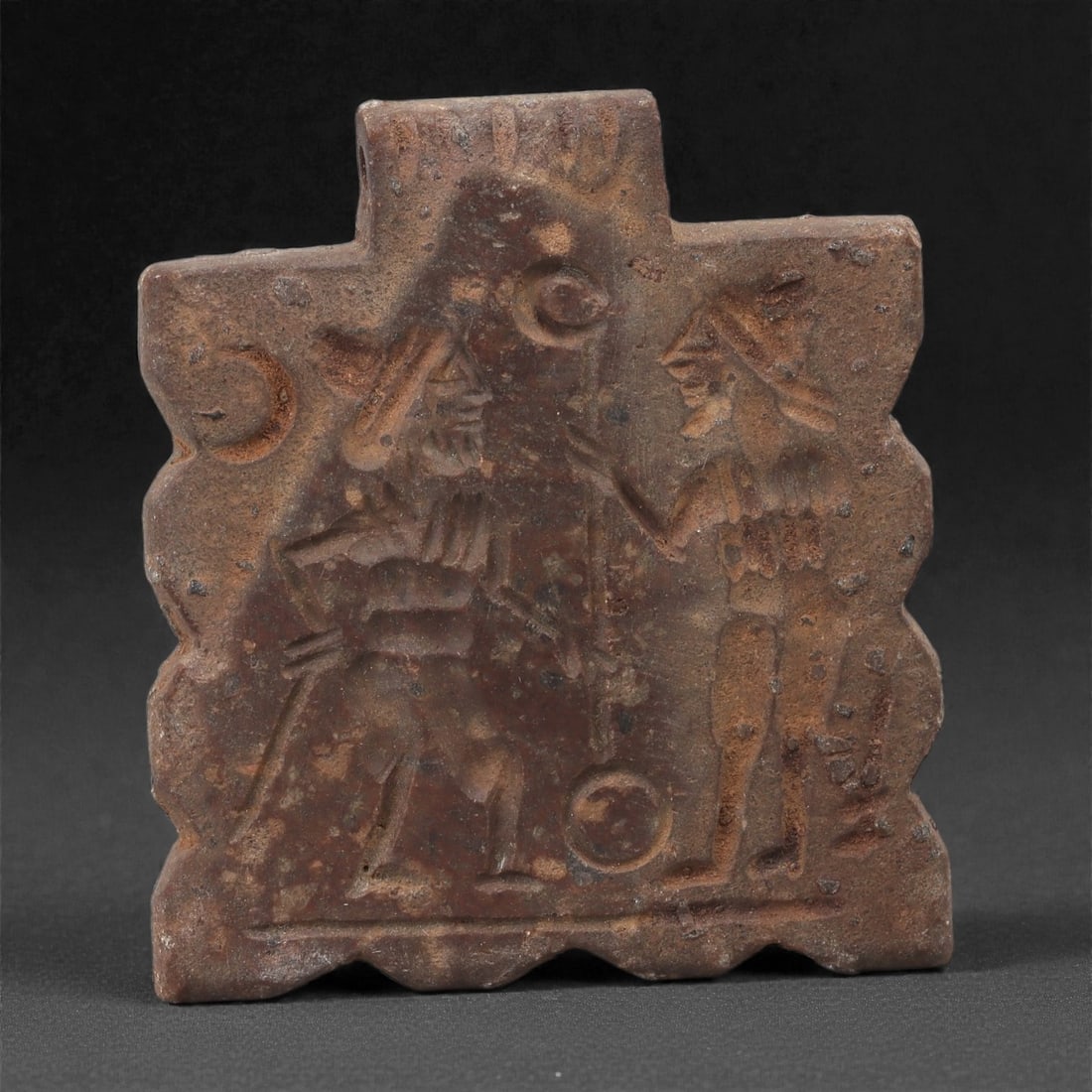 A Sasanian Stone Plaque Amulet, 3rd-7th Century CE, 33LR: Carved from a fine-grained stone with brown archaeological surface accretions, the amulet is shaped as a rectangular plaque with a scalloped perimeter and a narrow projecting tab at the top pierced fo