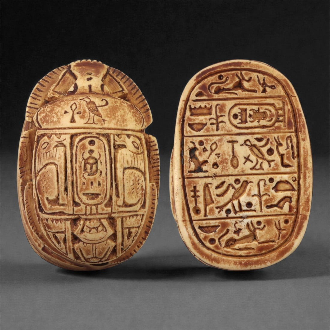 An Egyptian Royal and Mythological Limestone Scarab, 18th Dynasty, Circa 1550-1290 BCE, 38ZB: Carved from a pale limestone with areas of brown surface staining, the scarab displays a prominently modeled back with incised wing-case divisions and lateral leg detailing. The upper surface includes