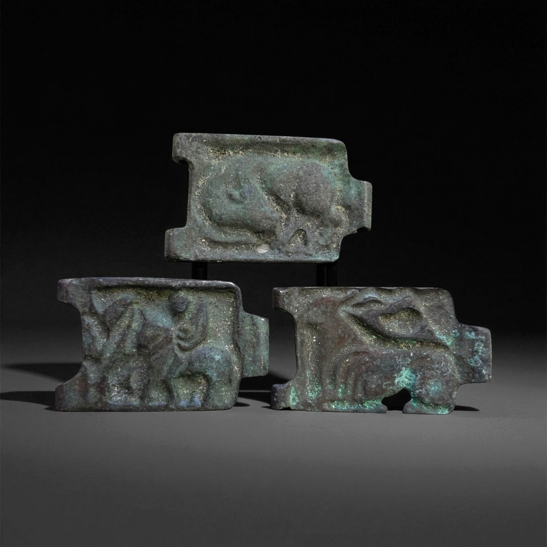 A Group of Three Sino-Scythian Bronze Belt Buckles, 3rd-1st Century BCE, 40 g, 39EE: Cast in bronze with a green patinated surface, each buckle is formed as a rectangular plaque with lateral notches for attachment. The relief decoration comprises zoomorphic motifs, including a recumbe