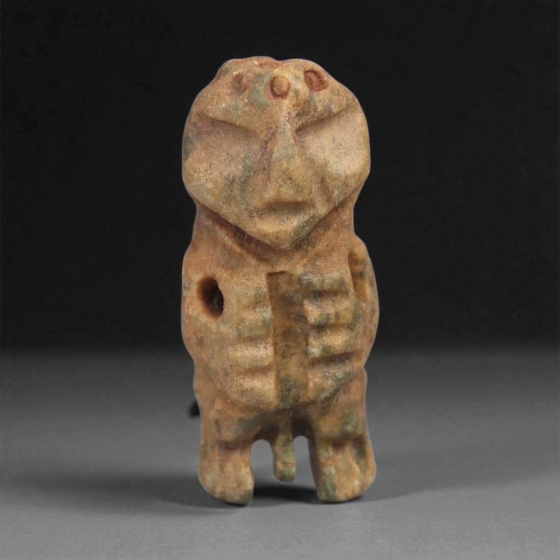 A Taino Carved Stone Idol, Late Ceramic Age, circa 1200-1500 CE, 83LD: Carved from mottled brown-green stone with areas of surface encrustation, the figure is shown standing with short bifurcated legs and a compact body. The head is rounded and bears recessed eyes, an in