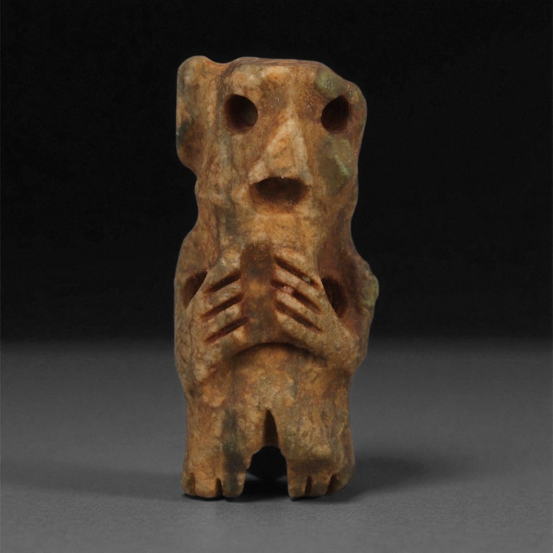 A Taino Carved Stone Idol, Late Pre-Columbian Period, Circa 1000-1500 CE, 71ZB: Carved from mottled brown stone with greenish surface areas, the figure stands upright with short legs and elongated arms held at the abdomen. The head is modeled with large drilled circular eyes, a s
