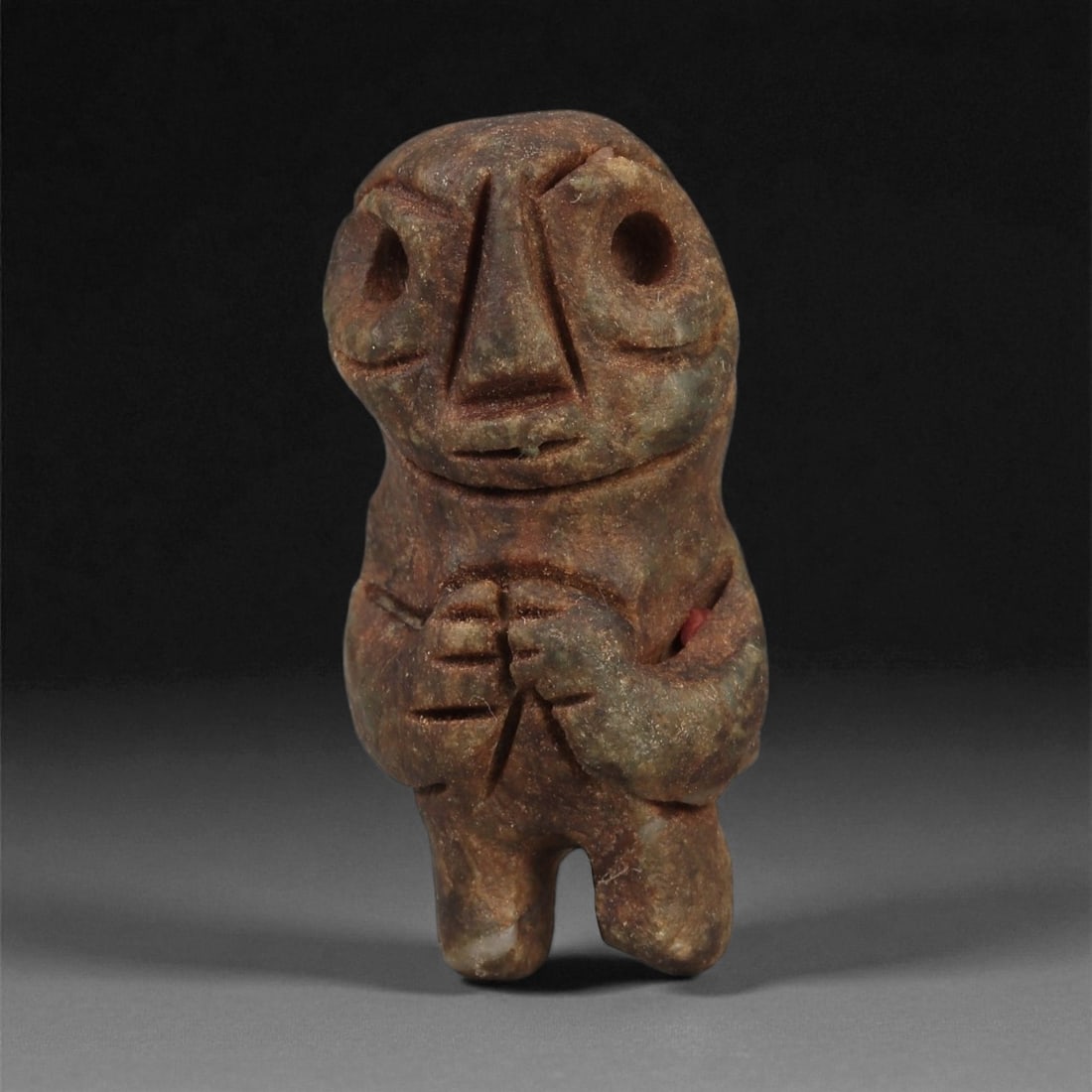 A Taino Carved Stone Idol, Late Pre-Columbian Period, Circa 1000-1500 CE, 88LF: Carved from a mottled brown-green stone with areas of lighter surface inclusions, the figure is shown standing with legs indicated by a narrow central groove. The torso bears a set of incised lines ac