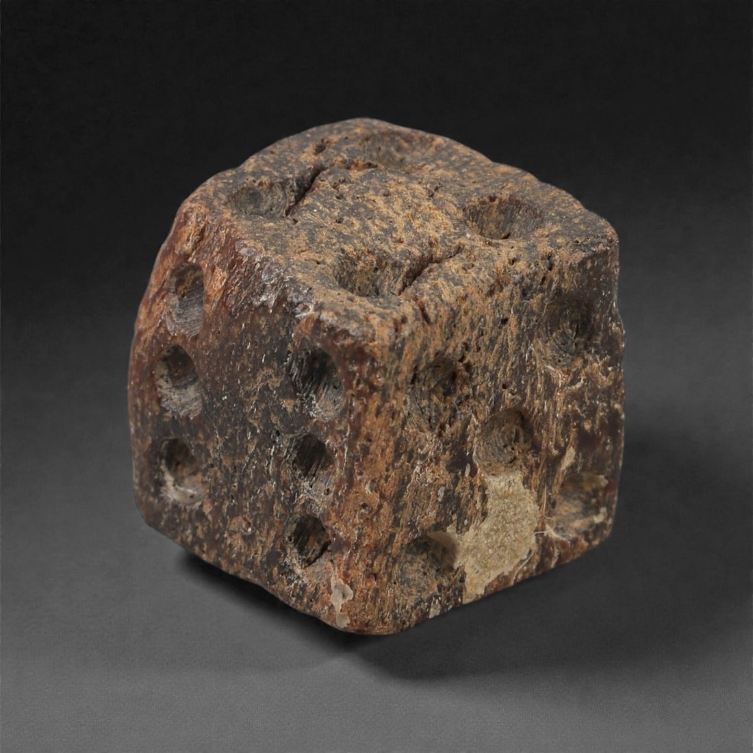 A Roman Bone Gaming Die, 1st-3rd Century CE, 1.5cm, 75A: Carved from dense bone, the object is shaped as a small cube with slightly rounded edges. Each face bears a series of drilled circular pips arranged in standard numerical configurations. The surfaces 