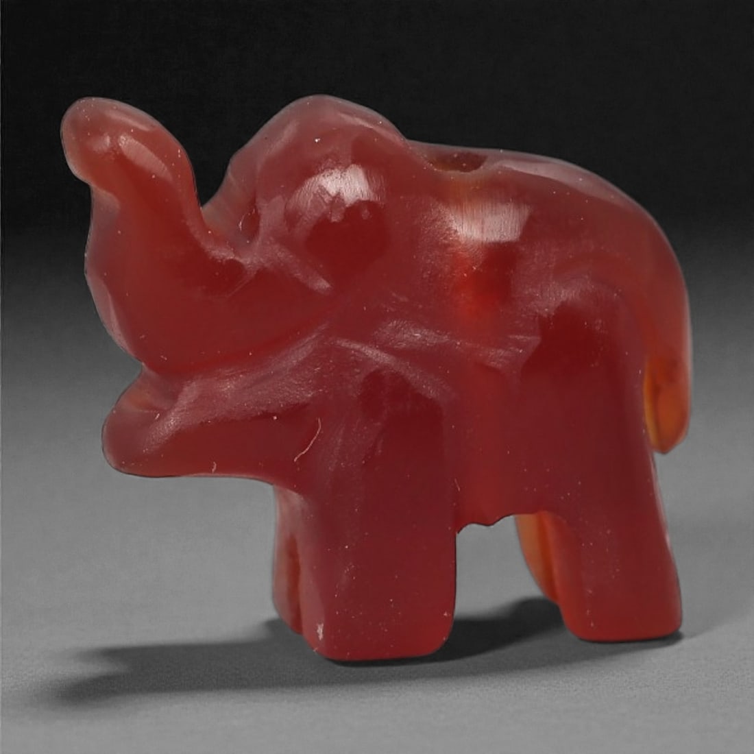 A Coptic Carnelian Elephant Amulet, 4th-7th Century CE, 78LS: Carved from deep red carnelian with lighter internal banding, the amulet depicts a stylized elephant with an upraised trunk, rounded head, and compact body supported by four straight legs. Shallow inc