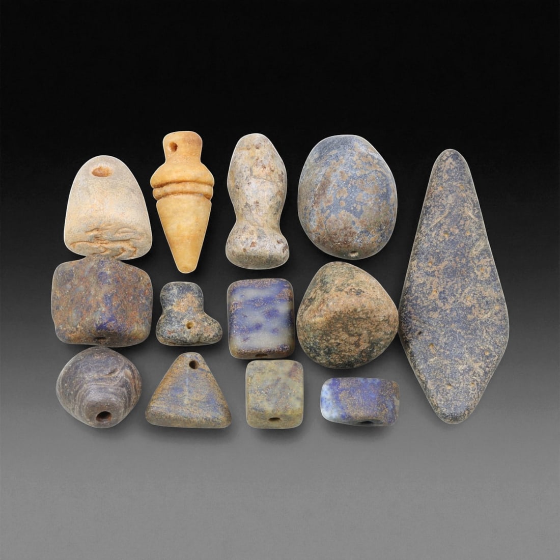 Ancient Mesopotamian Lapis Lazuli and Stone Amulet Beads, c. 3rd-2nd Millennium BCE, 1-5.7cm, 34EL: This diverse assemblage of ancient amulets and beads, carved from lapis lazuli, alabaster, and various hardstones, reflects the devotional and ornamental artistry of early Mesopotamian civilization. T