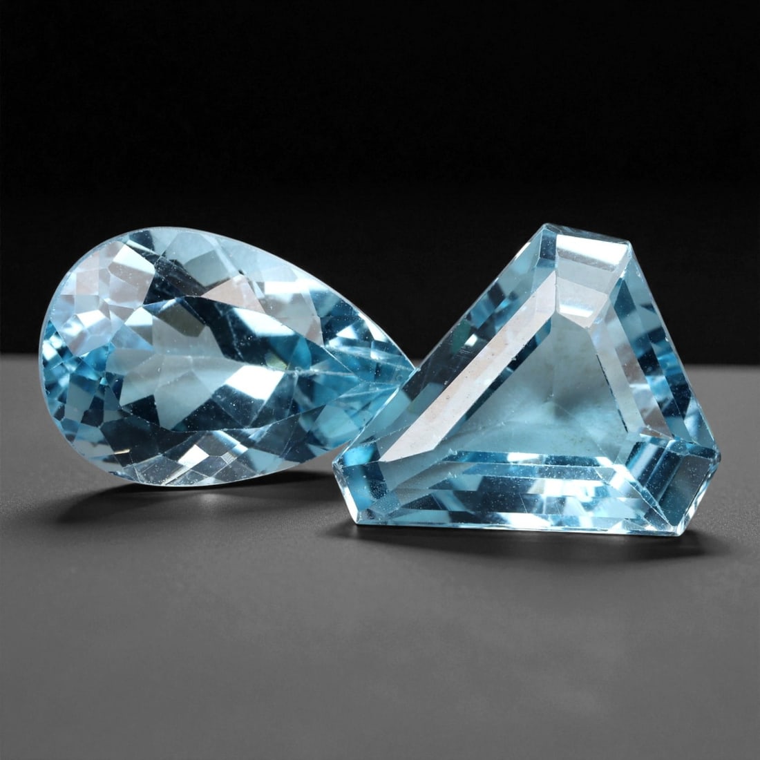 14.95 Carats Sky Blue Topaz Pair - Natural Brazilian Stones - 1.9 cm, 11XE: This striking pair of sky blue topaz gems glows with crystal clarity and icy brilliance. One pear-cut and one trillion-cut, they showcase precision faceting and a cool, refreshing tone that sparkles e