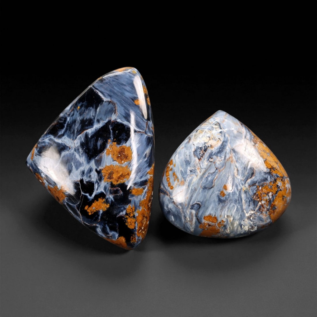 66.05 Carats Pietersite Cabochon Pair - Natural Freeform Shields, 3.1 x 2.2 cm, 87XE: This captivating pair of Pietersite cabochons showcases the stone's signature tempest-like movement, with dramatic swirls of inky blue, slate gray, and fiery ochre coursing through each polished surfa