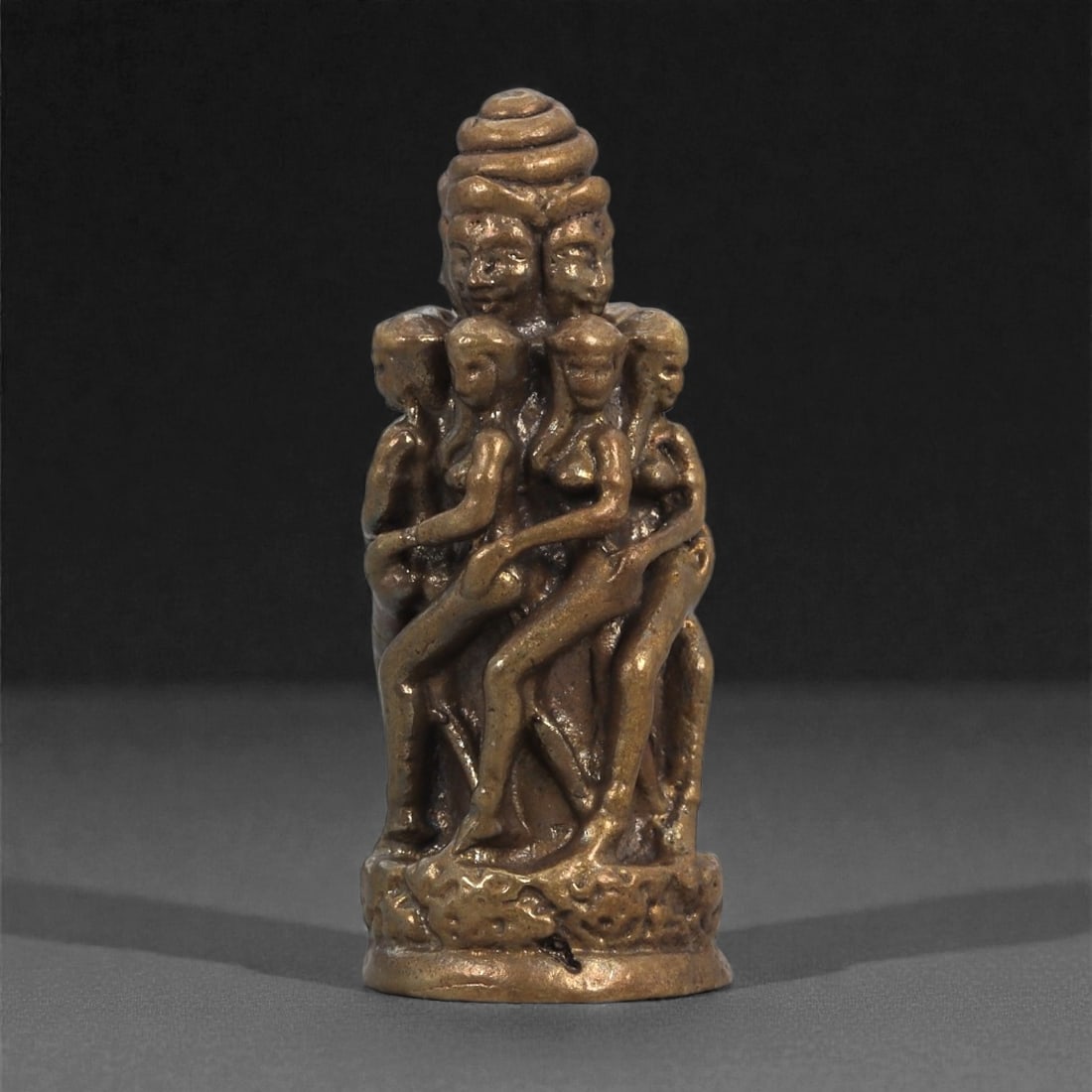 Bronze Multi-Figure Erotic Column - Southeast Asian Ritual Idol, 4D: Cast in bronze with a warm, muted sheen, this miniature sculpture forms a vertical column of entwined female figures surrounding a central core surmounted by a multi-faced head. The bodies are elongat